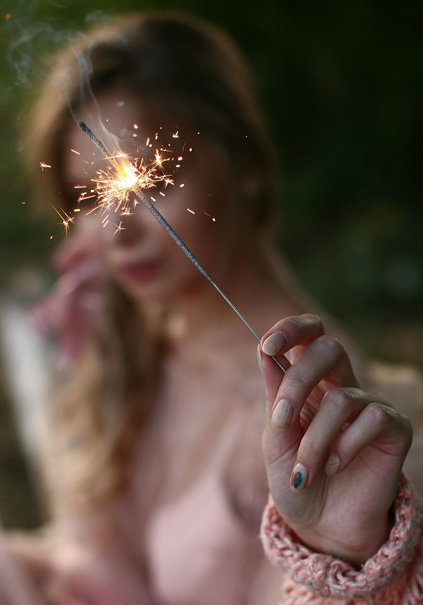 Mulher segurando uma fagulha acesa, a luz iluminando o rosto.